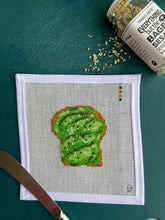 Load image into Gallery viewer, Green plastic chopping board backgrounders on which rests a white needlepoint canvas stitched with vivid greens depicting a realistic avocado toast with beaded salt and pepper
